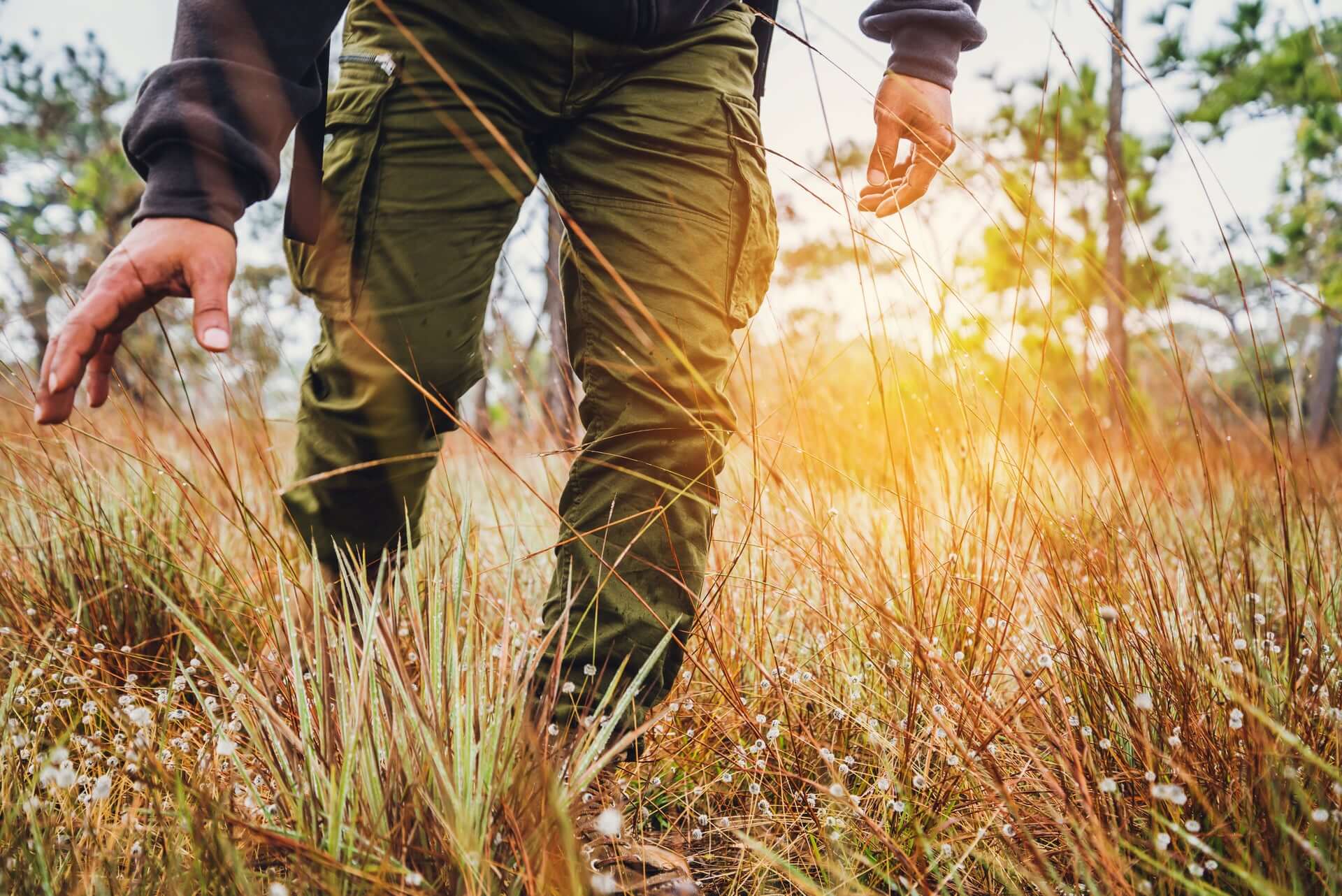 Man in outdoor cargo pants walking through grass during camping trip, highlighting comfort and style for travel adventures.