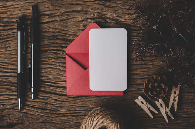 Flat lay of a blank gift card on a red envelope with pens and decorative items on a wooden table.