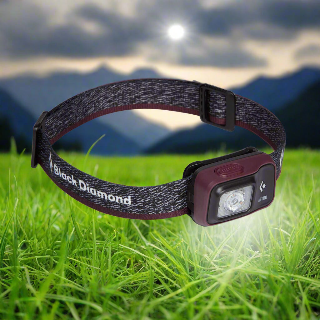 Black Diamond Astro 300 LED head torch in black and burgundy on green grass, ideal for outdoor camping adventures.