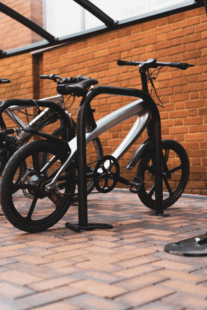 Sleek carbon black e-bike parked at a bike rack, showcasing its modern design and outdoor adventure appeal.