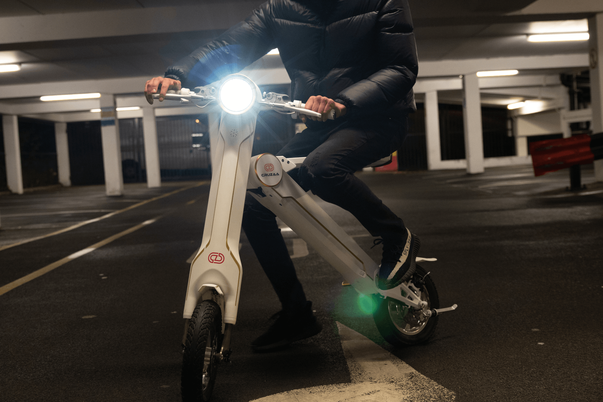 Rider using the limited edition Cruzaa electric scooter with a headlight in a dimly lit parking area, showcasing urban adventure.