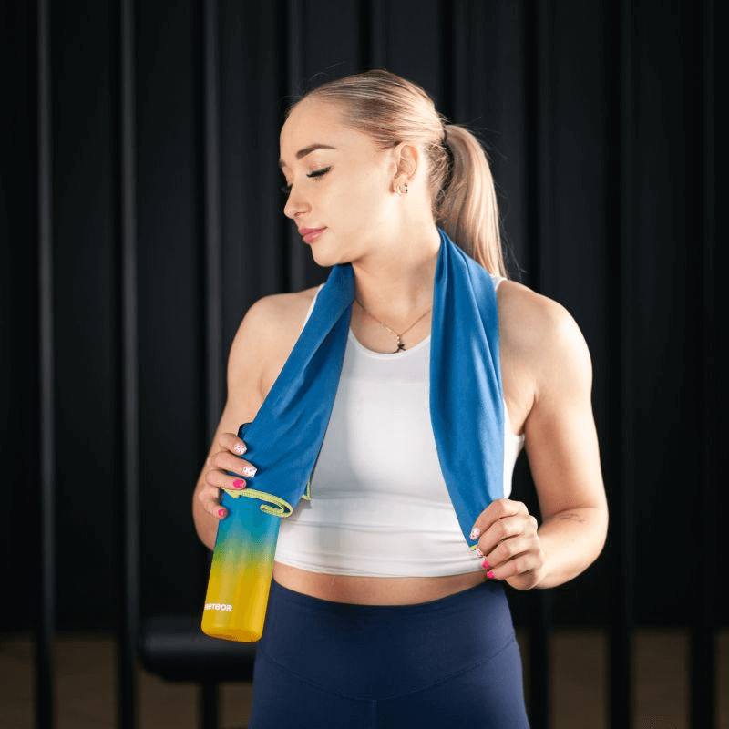 Woman wearing a blue microfiber towel around her neck, holding a water bottle, ideal for sports and outdoor activities.