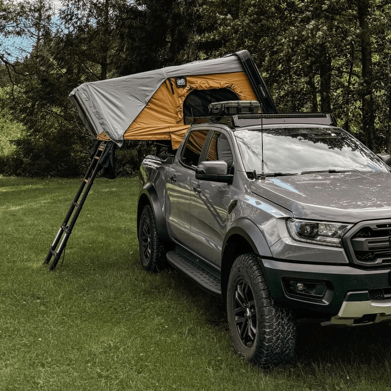 Offlander Fold 2 Sand Roof Tent mounted on a grey truck in a grassy outdoor setting, perfect for adventure travel.