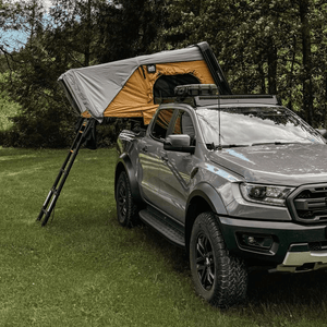 Offlander Fold 2 Sand Roof Tent mounted on a grey truck in a grassy outdoor setting, perfect for adventure travel.