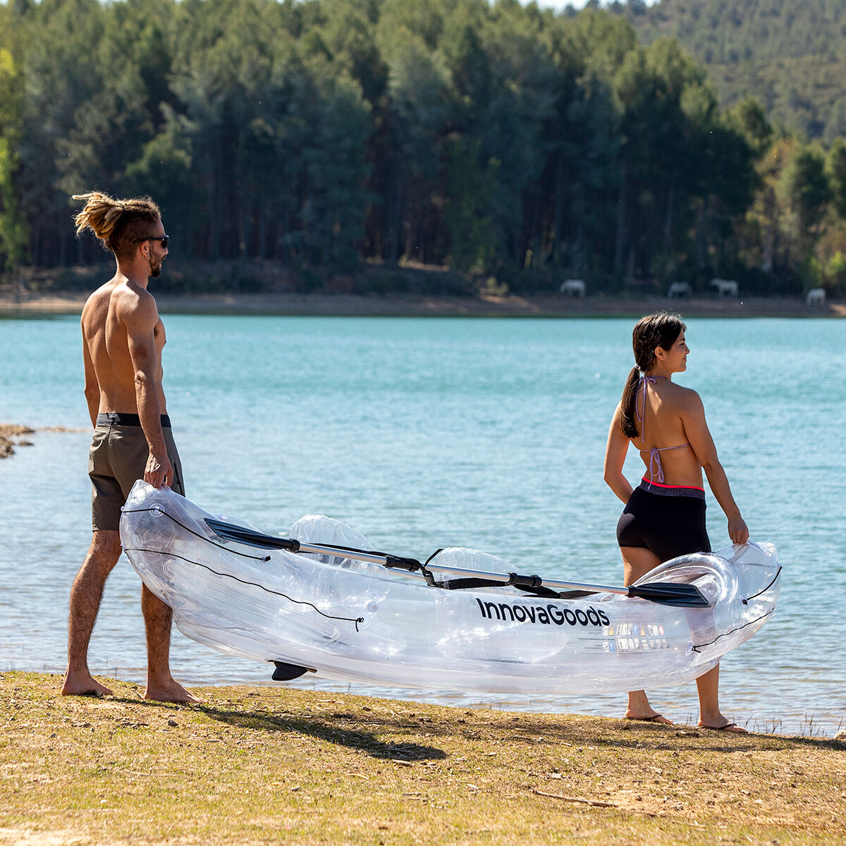 Couple carrying Inflatable Transparent Kayak by InnovaGoods at a lake, perfect for outdoor camping adventures.