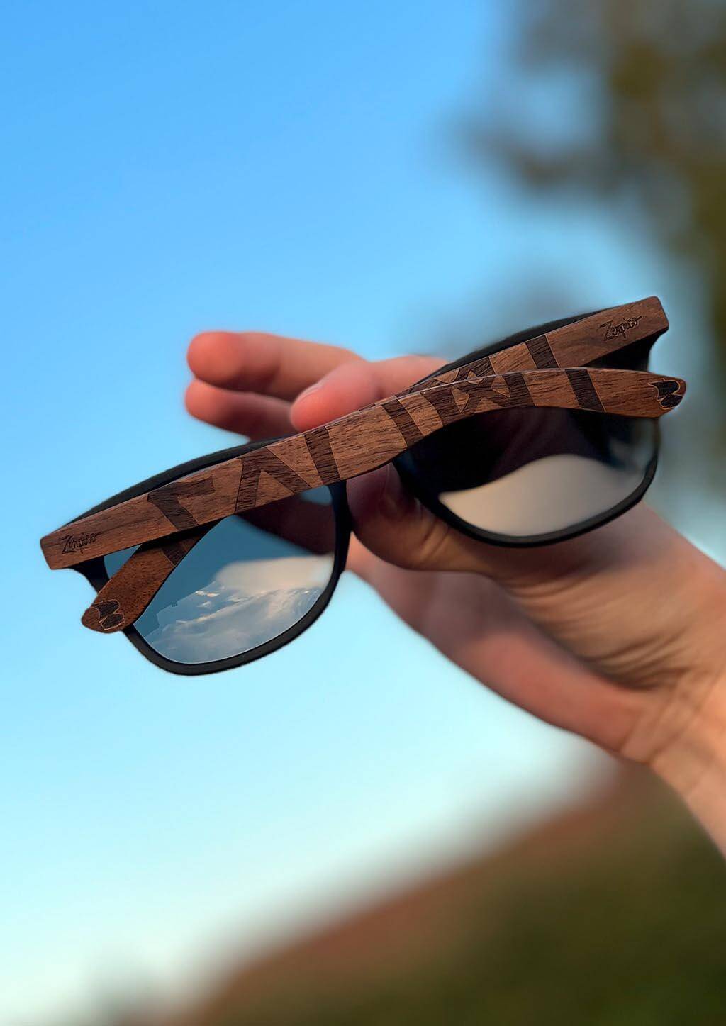 Hand holding Eyewood engraved wooden sunglasses featuring Viking runes outdoors, ideal for adventure and camping.