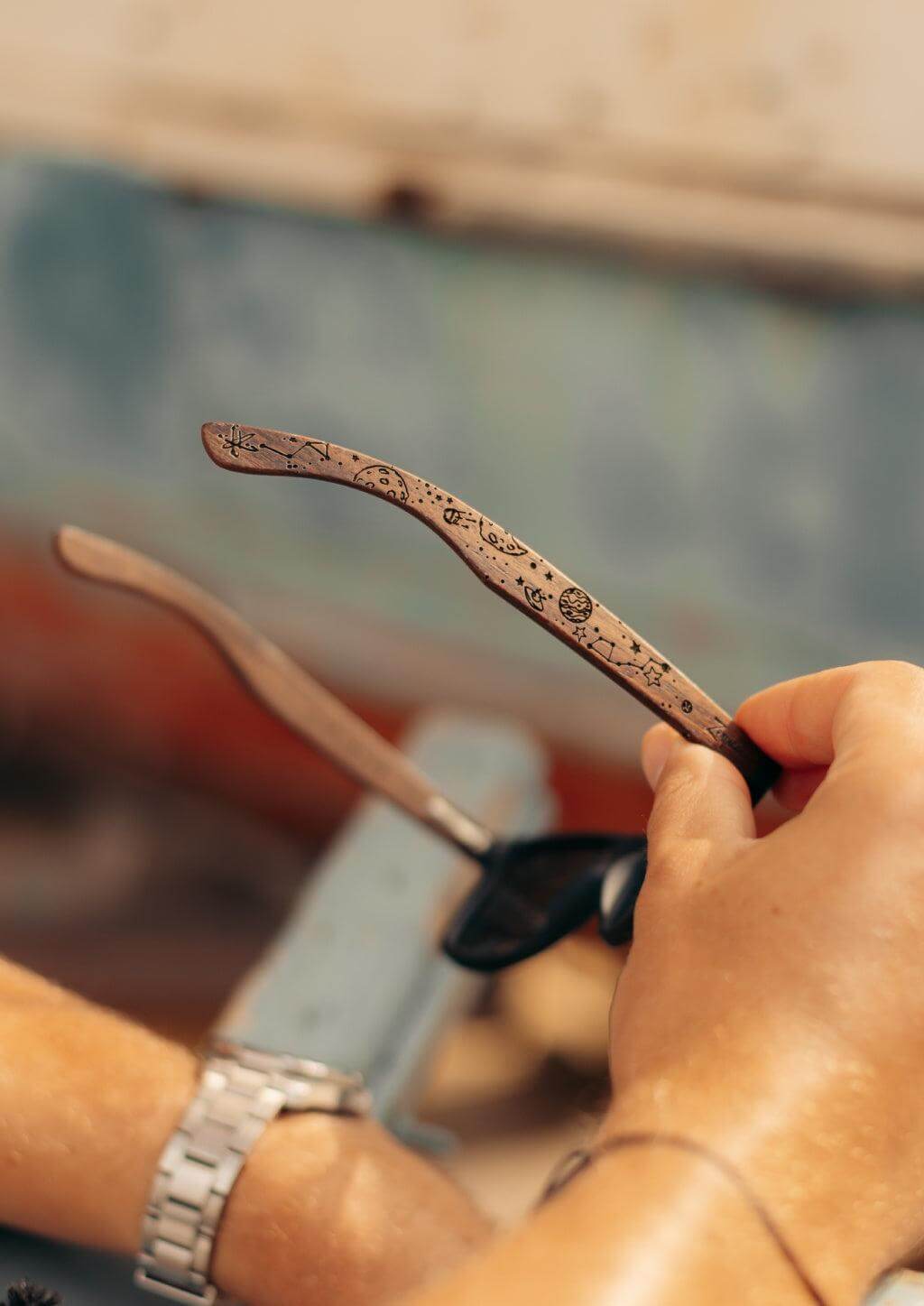 Person holding engraved wooden sunglasses with intricate designs, showcasing outdoor adventure style.