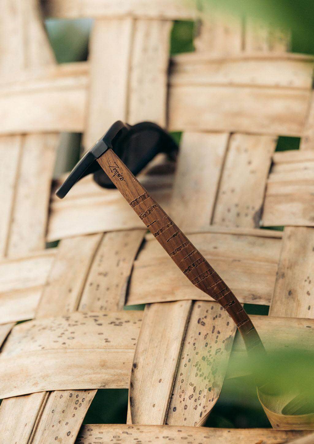 Engraved wooden sunglasses arm resting on a woven basket, showcasing unique design for outdoor adventures.