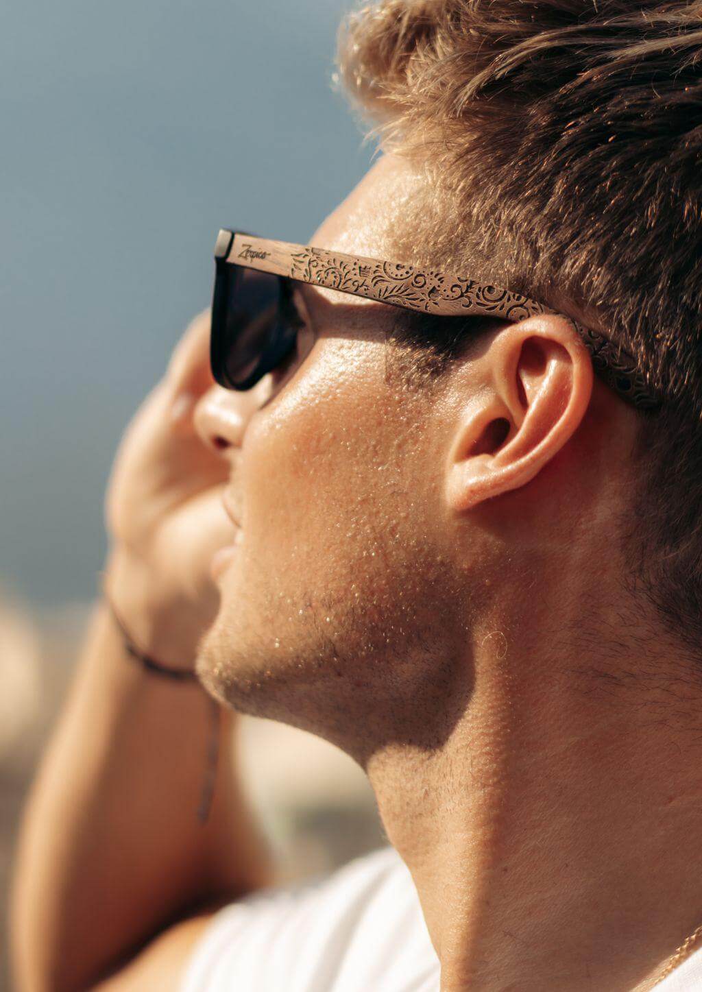 Man wearing engraved wooden sunglasses outdoors, showcasing a flower pattern, perfect for adventure and camping.