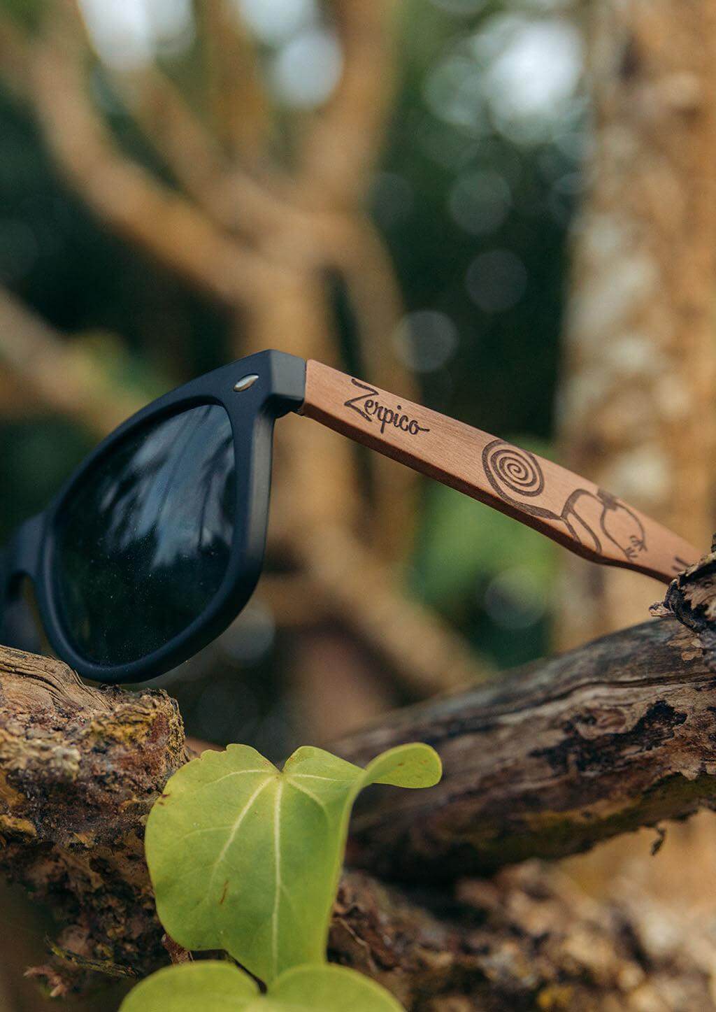 Handmade wooden sunglasses with engraved temples resting on tree branches, perfect for outdoor adventures.